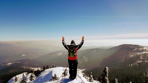 Full length rear view of man with arms raised standing on mountain against sky