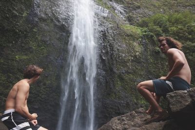 Young couple sitting on rock by waterfall