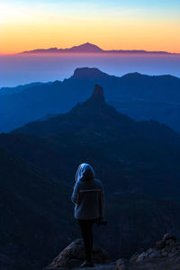 Rear view of man standing on mountain during sunset