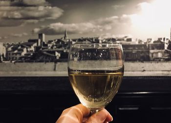 Close-up of hand holding drink by river against sky