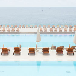 Lounge chairs by swimming pool by sea against sky