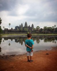 Rear view of boy standing on shore against sky