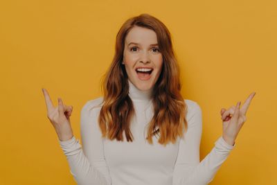 Portrait of young woman gesturing against yellow background