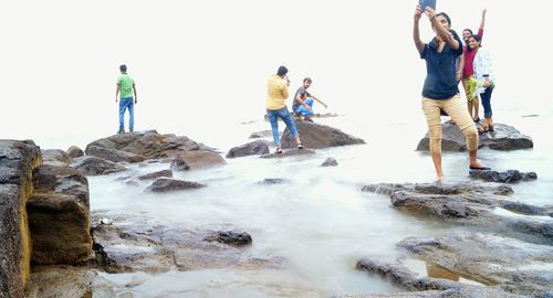 People standing on rocks in water against sky