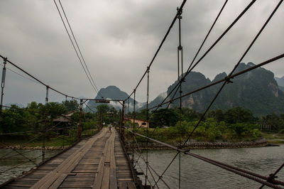 Footbridge over river against silhouette of mountain