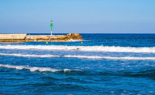 Lighthouse by sea against clear blue sky