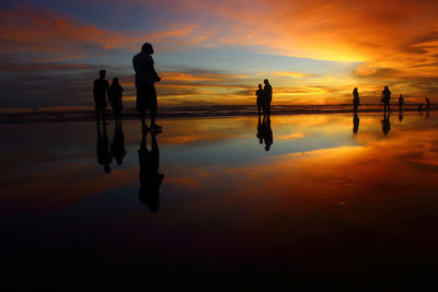 Silhouette people on beach against orange sky