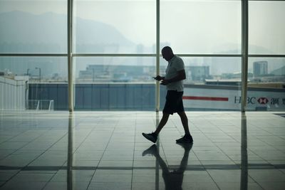 Rear view of man walking on glass window at airport