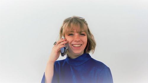 Portrait of smiling young woman talking smart phone while standing against white background