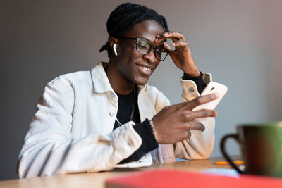 Successful smiling african american man holding phone uses entertaining mobile apps or social media