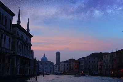 Canal amidst buildings in city at sunset