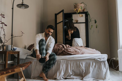 Man wearing sock with non-binary person standing near wardrobe in bedroom at home