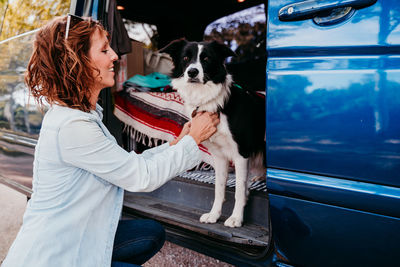Side view of smiling woman holding dog in camper trailer