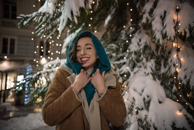 Smiling woman standing against illuminated tree during winter