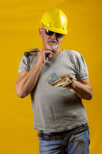 Portrait of young man standing against yellow background