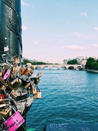 Padlocks on bridge over river against sky