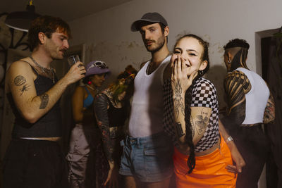 Portrait of happy non-binary person blowing kiss with friends celebrating during party in apartment