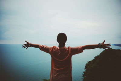 Rear view of woman with arms outstretched against sea