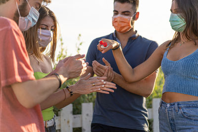 Group of young people wearing protective mask using sanitizing gel together against the coronavirus