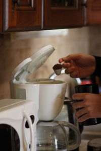 The man's hands hold a coffee grinder and spoon coffee into the coffee maker.