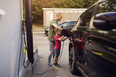 Father and son charging electric car by house