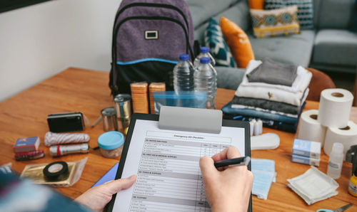 Unrecognizable woman doing checklist of emergency backpack in the living room