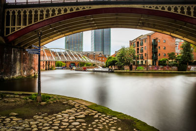 Bridge over river by buildings against sky