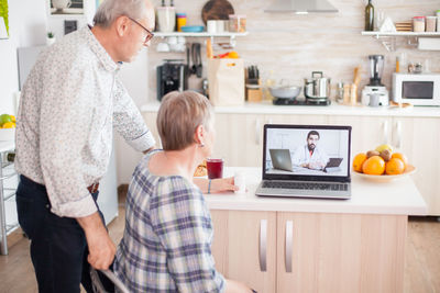 Rear view of man using laptop on table at home