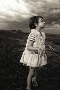 Girl imitating zombie on field against cloudy sky