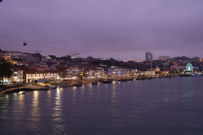 Illuminated buildings by river against sky at dusk