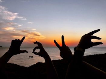 Silhouette hands gesturing at beach against sky during sunset