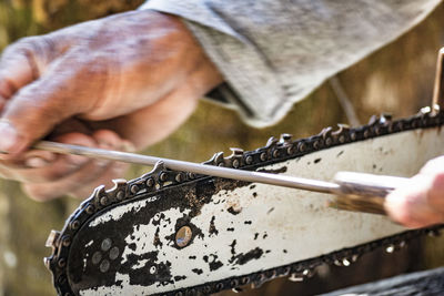 Close-up of hands using a file to sharpen a chainsaw blade
