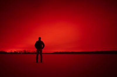 Silhouette of man standing on red landscape against sky at sunset