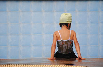 Rear view of woman wearing hat sitting on floor against wall