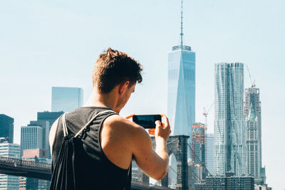 Rear view of man photographing city against clear sky