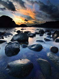 Rocks at sea shore against sky during sunset