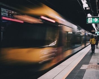 Blurred motion of train by people walking at railroad station platform