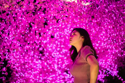 Low angle view of woman standing against illuminated tree at night