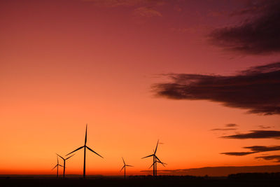 Low angle view of silhouette wind farm against orange sky