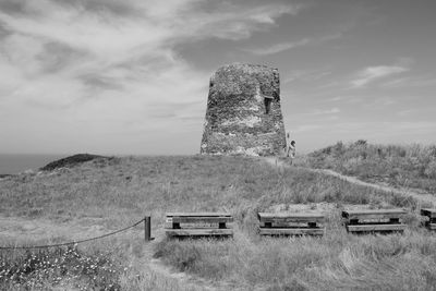 Traditional windmill on field by sea against sky