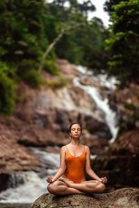 The girl sits in a lotus position on the background of a waterfall