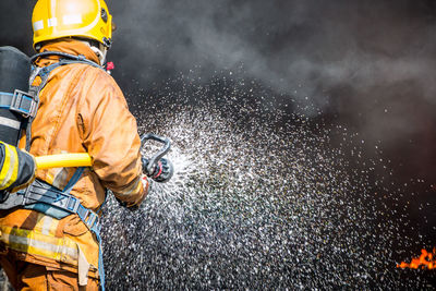 Rear view of firefighter spraying water on fire