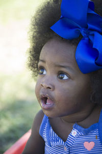 Close-up of cute baby girl with blue bow tied on curly hair