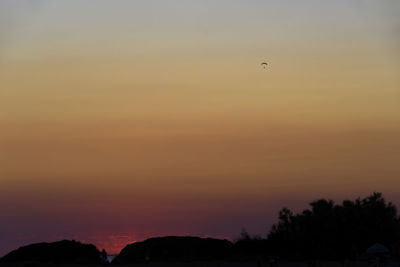 Silhouette of birds flying against orange sky