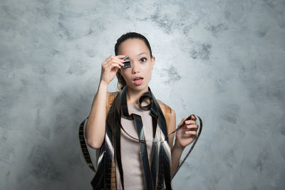 Portrait of woman holding little clapperboard while standing against wall