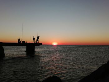 Silhouette family fishing in sea during sunset