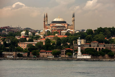 Strait by buildings and mosques against cloudy sky