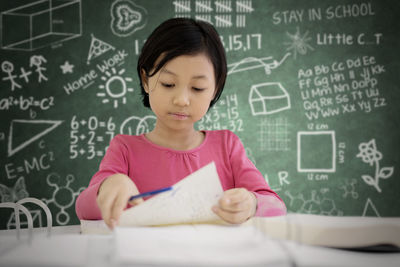 Girl studying at table against bookshelf