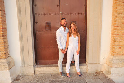 Portrait of young couple standing against closed door of historic building