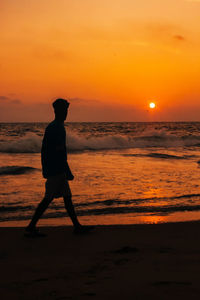 Silhouette man standing on beach against orange sky